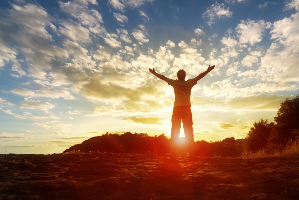Silhouetted figure with arms outstretched against a vibrant sunset sky, symbolizing freedom and inspiration. Ideal for themes of empowerment or nature.